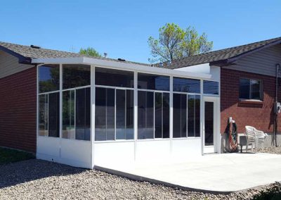White aluminum sunroom with high ceilings, glass walls, concrete patio