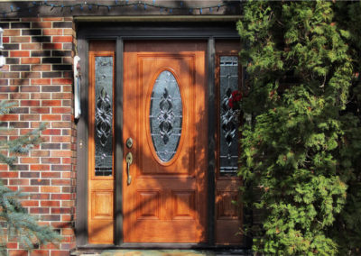A vibrant medium stained wood door on a brown brick house.