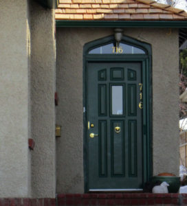 A green door on a stucco house with a little window above the door.